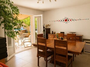 A dining area with a wooden table and chairs, a decorative wall piece, and a view of the outdoor patio. - L'Oliveraie Quiet villa with pool at the gateway to the Luberon. (Pertuis)