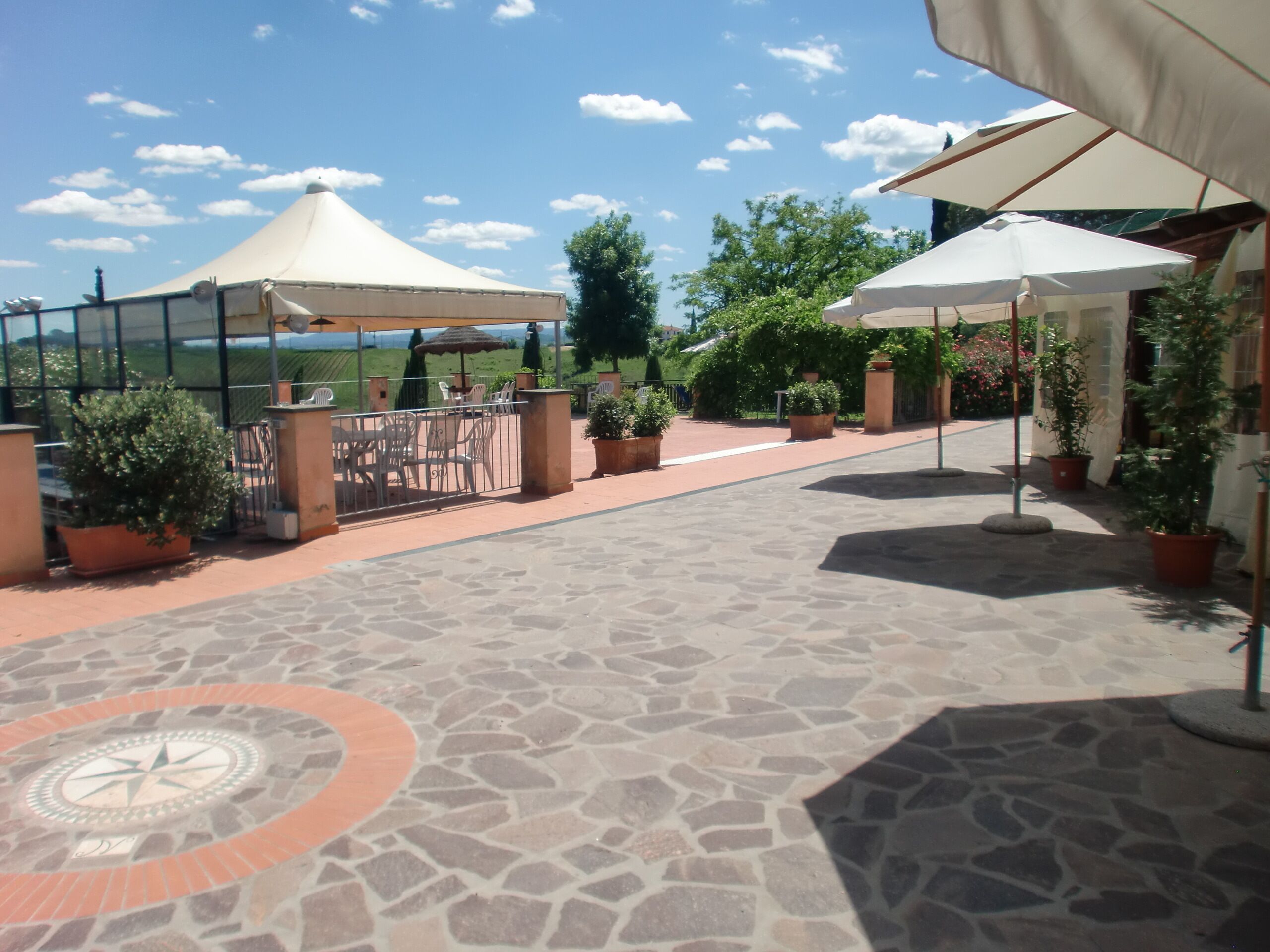 An outdoor patio with stone flooring, potted plants, and umbrellas providing shade.