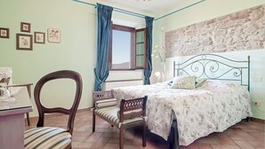 A bedroom with a bed, a chair, a desk, a window with curtains, and a stone wall. - Agriturismo Tenuta Isola Verde (Cerreto Guidi)