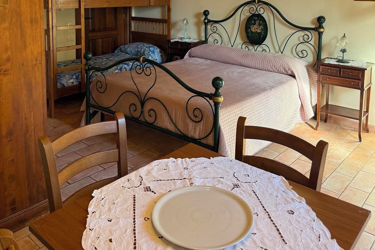 Een slaapkamer met een stapelbed, een eenpersoonsbed, een tafel met een bord en een stoel.
