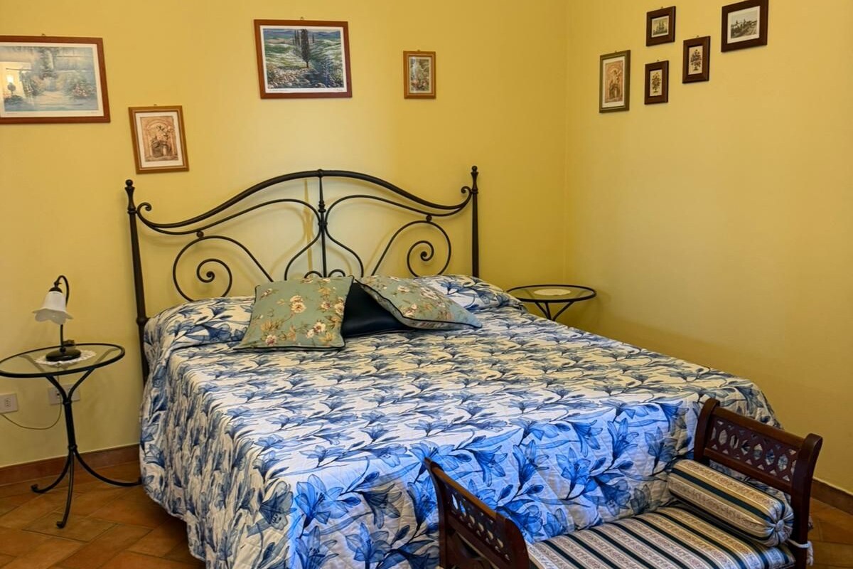 Een slaapkamer met een bed, een stoel, een nachtkastje, een lamp en een kroonluchter.