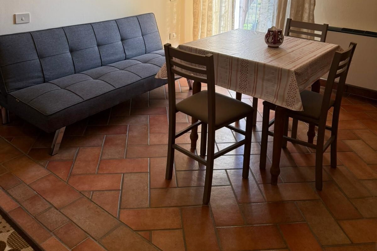 Een eethoek met een tafel, stoelen, een bank, een kroonluchter en een stenen muur.