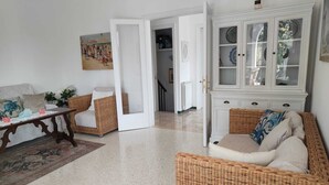 Un salón con muebles de mimbre, un armario blanco con puertas de cristal y un cuadro en la pared.