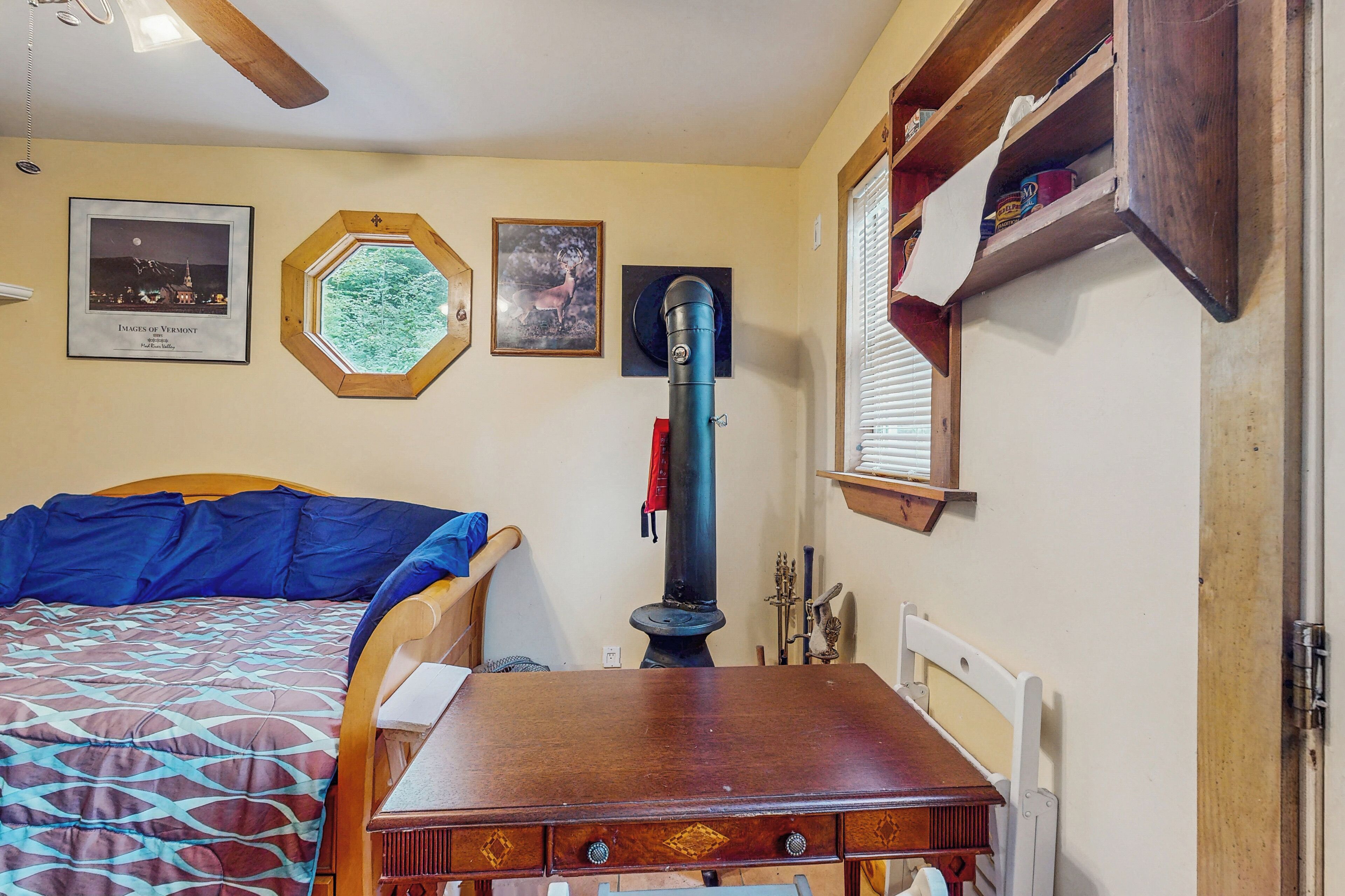 A bedroom with a bed, a wooden dresser, a heater, and framed pictures on the wall.