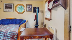 A bedroom with a bed, a wooden dresser, a heater, and framed pictures on the wall. - Tiny House at Sugarbush North: Adventure Hub! (Waitsfield)