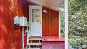 A red wooden house with a white door, a small porch, and a utility box on the left. - Tiny House at Sugarbush North: Adventure Hub! (Waitsfield)