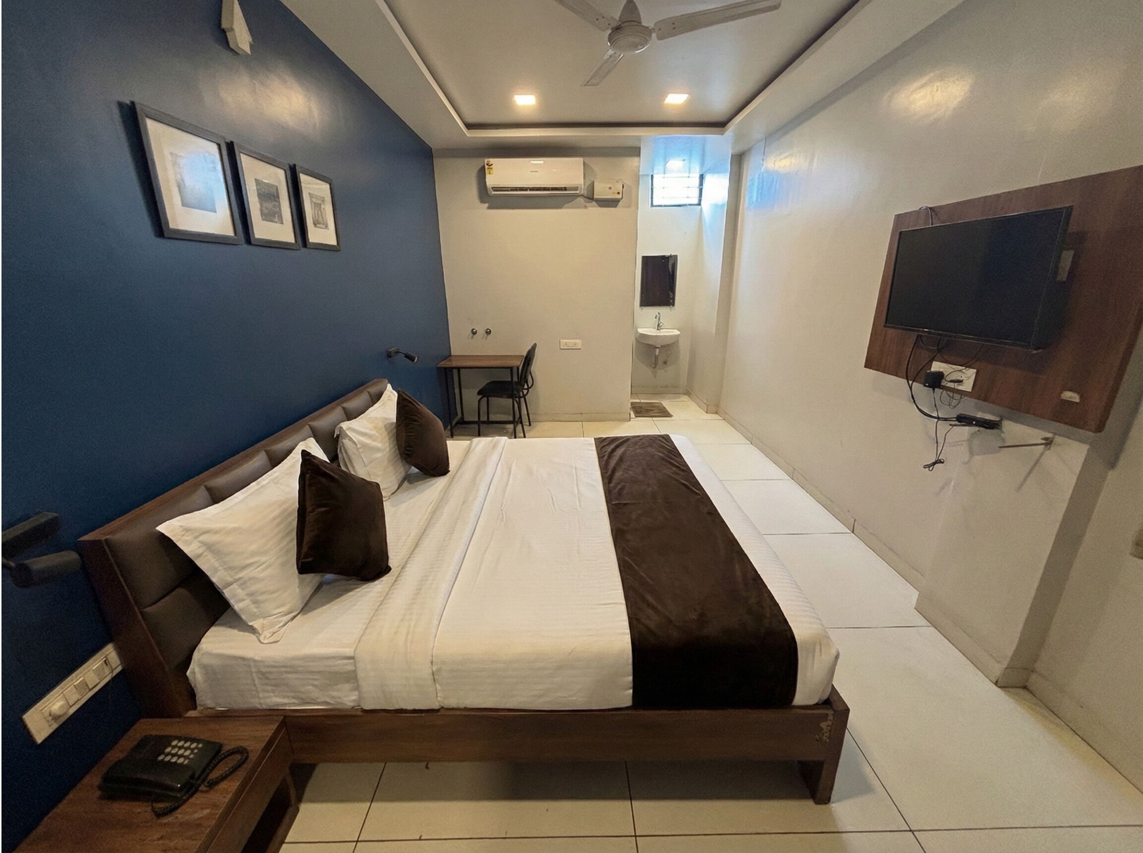 A hotel room with a bed, a desk, a chair, a TV, and an air conditioning unit.