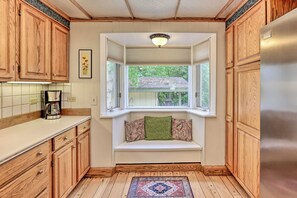A kitchen with wooden cabinets, a built-in bench with pillows, a window, and a refrigerator.