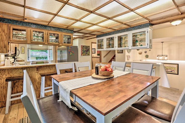 A dining area with a wooden table, white chairs, and a kitchen with wooden cabinets and a tiled backsplash.