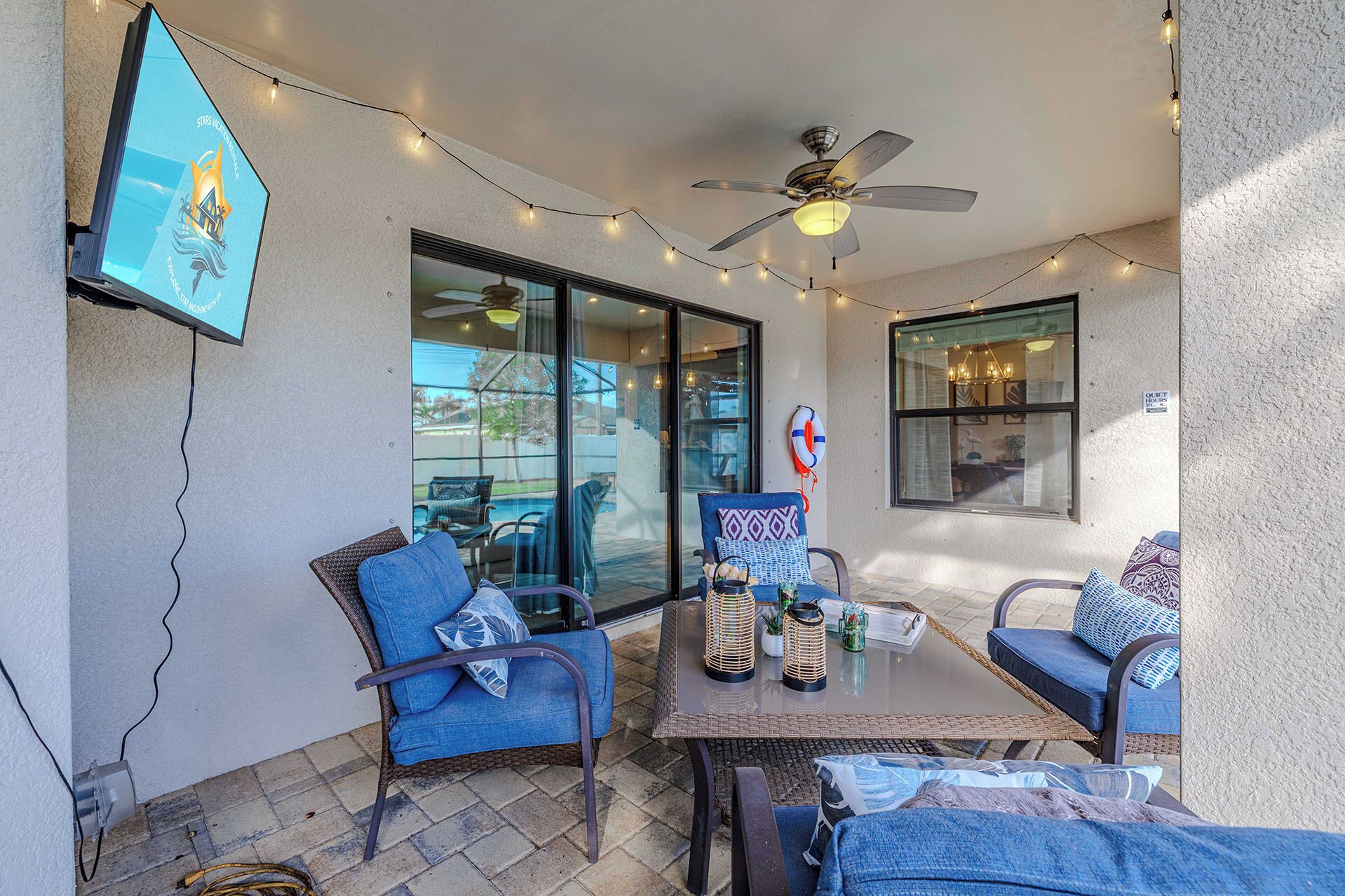 An outdoor patio with wicker furniture, string lights, and a ceiling fan.
