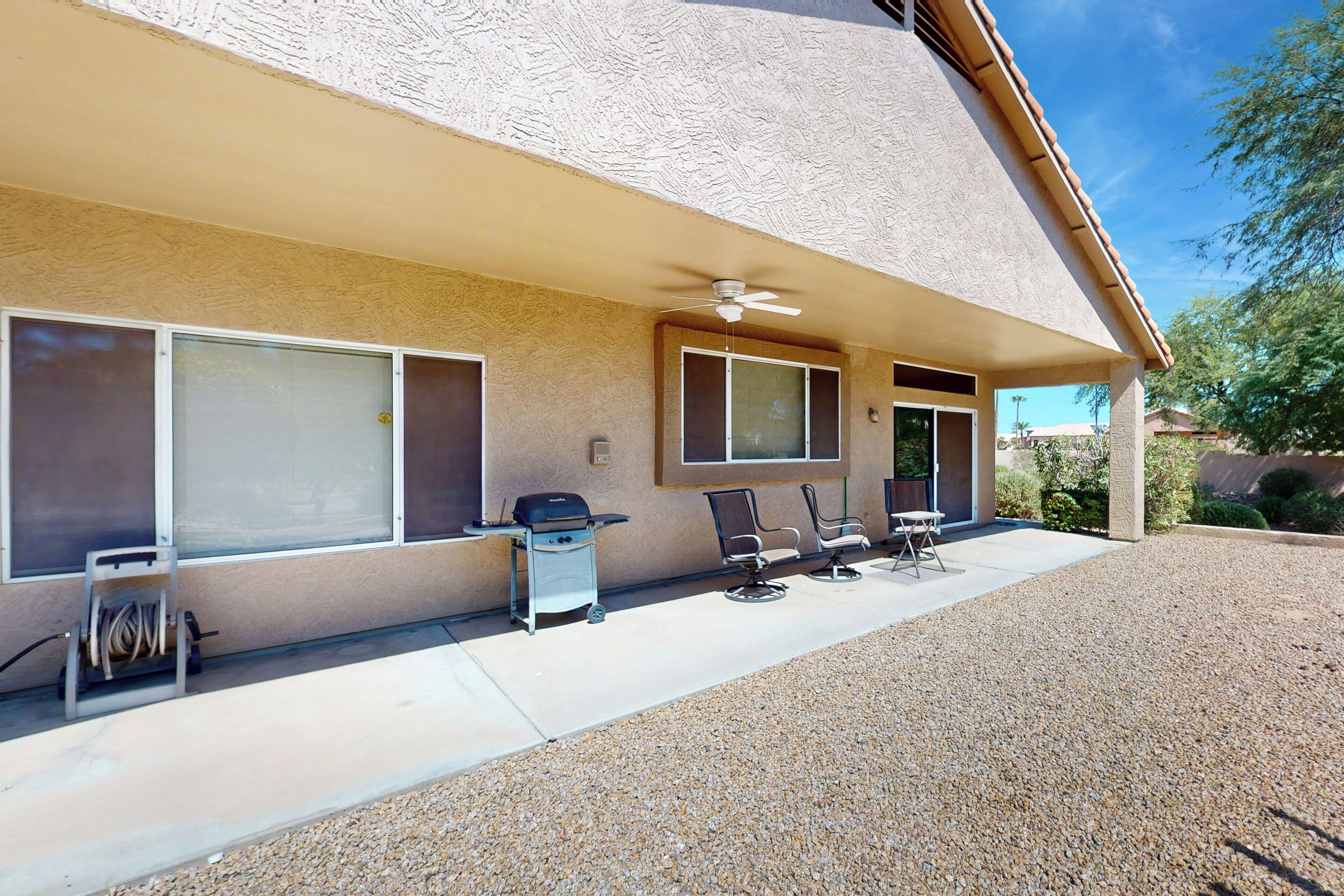 A house with a covered patio, a ceiling fan, and a grill.