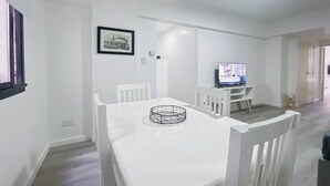 A modern dining area with a white table and chairs, a framed picture on the wall, and a television in the background. - Charming Apartment in Recoleta 4 Paxa (Buenos Aires)