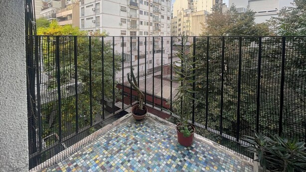 A balcony with a tiled floor, a potted plant, and a view of surrounding buildings. - Charming Apartment in Recoleta 4 Paxa (Buenos Aires)