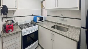 A compact kitchen with white cabinets, a gas stove, a microwave, and a sink. - Charming Apartment in Recoleta 4 Paxa (Buenos Aires)