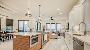 Una cocina moderna con una isla central, hornos empotrados, un amplio ventanal y un ventilador de techo.