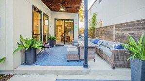 Un patio al aire libre con mobiliario de mimbre, ventilador de techo y plantas en macetas.