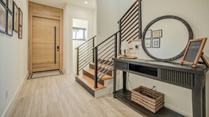 Una escalera con detalles de madera y barandillas metálicas, una consola con espejo y cuadros enmarcados, y una puerta con panel de madera.