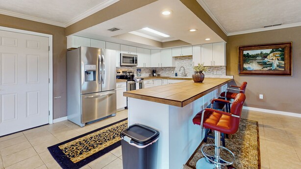 Una cocina moderna con electrodomésticos de acero inoxidable, una isla central con taburetes de bar y un cuadro en la pared.
