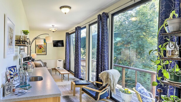 A modern kitchen with a built-in island, a dining area with a wooden table, and a balcony with potted plants. - Walk to Cafes! Storybook-Style Fairbanks Studio (Fairbanks)