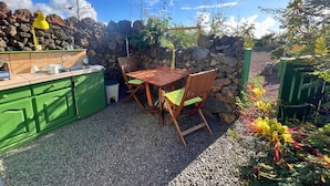 Uma área de cozinha externa com mesa e cadeiras de madeira, pia e luminária amarela.