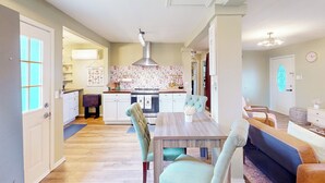 Eine moderne Küche mit Kochinsel, ein Essbereich mit Holztisch und Stühlen sowie ein Wohnzimmer mit Sofa und Couchtisch.