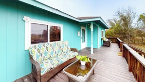 Ein türkisfarbenes Haus mit Veranda, einem Korbssessel und einem Blumentopf.
