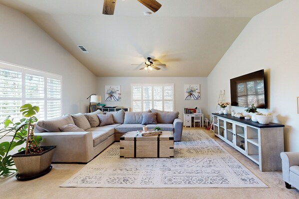 A spacious living room with a large L-shaped sofa, a coffee table, and a television on a cabinet.
