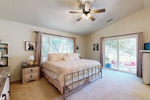A bedroom with a bed, bedside tables, a ceiling fan, and large windows.