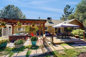 A backyard with a hot tub, wooden pergola, outdoor seating, and potted plants.