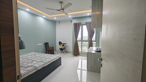 A bedroom with a bed, a ceiling fan, a window with curtains, and a desk with a scale. - 3bhk fully furnished highrise apartment in a luxerious complex with lake view (Kolkata)