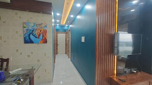 A hallway with a modern design, featuring a colorful painting on the left wall, a wooden panel on the right, and a television mounted on the wall. - 3bhk fully furnished highrise apartment in a luxerious complex with lake view (Kolkata)