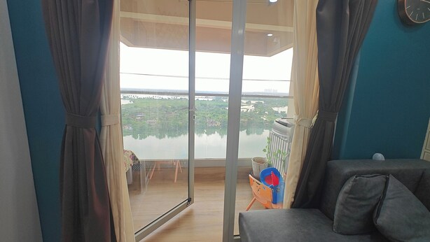 A balcony with a view of a lake and buildings, a sofa, and a small table with a chair. - 3bhk fully furnished highrise apartment in a luxerious complex with lake view (Kolkata)