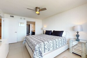 A bedroom with a bed, bedside tables, a ceiling fan, and a door. - All-Suite Coastal Retreat: Suntide III - Unit 405 (South Padre Island)