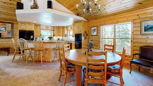 L’intérieur d’une cabane en rondins, avec une table à manger centrale, des chaises en bois, un lustre et une cheminée.