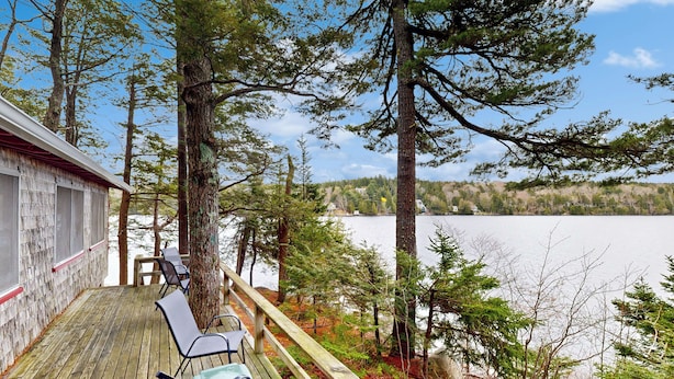 A wooden deck with chairs overlooking a lake, surrounded by trees. - Peaceful 2BR Lakefront Cabin w/ New Dock (Mount Desert)