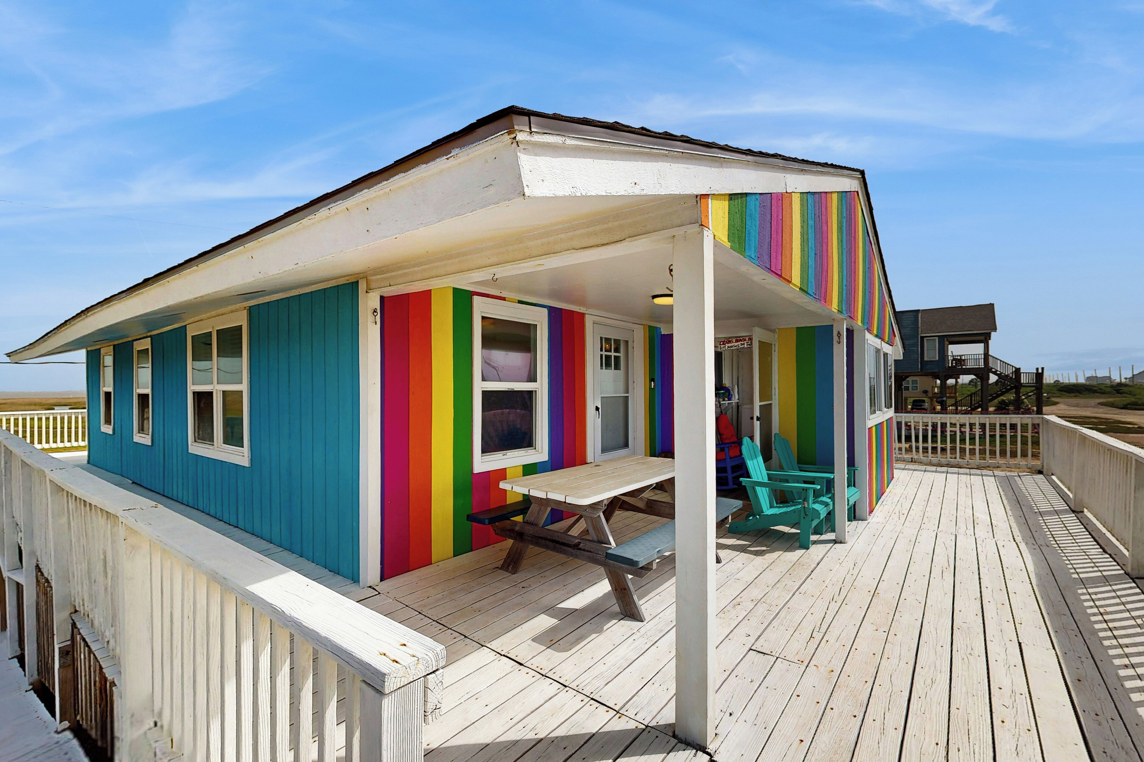 A colorful beach house with a wooden deck and picnic table.