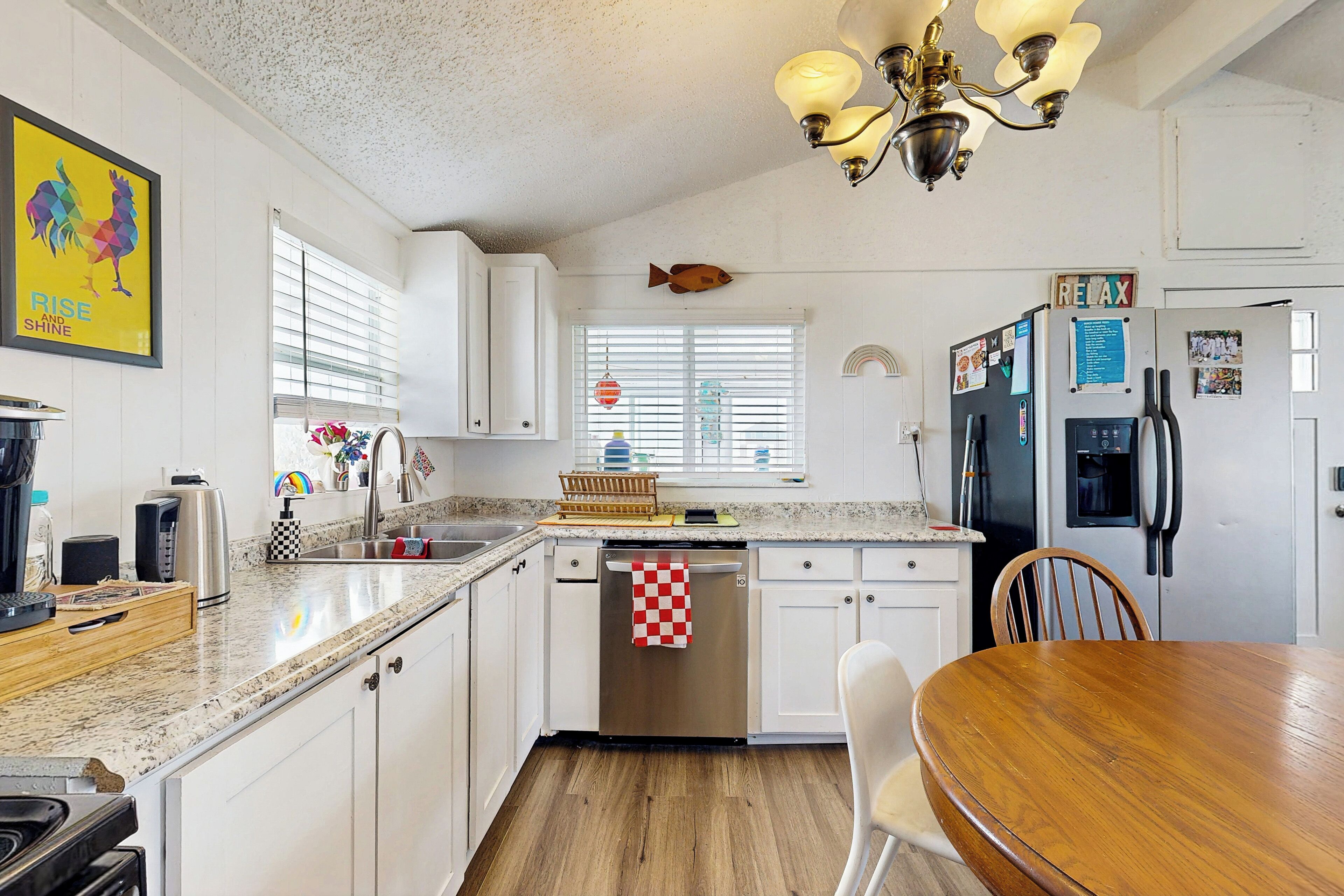A kitchen with white cabinets, a stainless steel dishwasher, a wooden dining table, and a fish hanging on the wall.