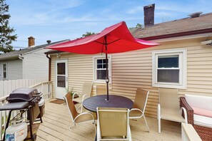 Une terrasse avec une table ronde et des chaises, un parasol rouge et un barbecue.