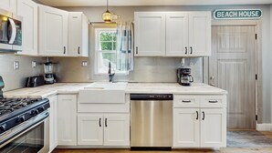 Une cuisine moderne avec des meubles blancs, un lave-vaisselle, une cuisinière et une machine à café.