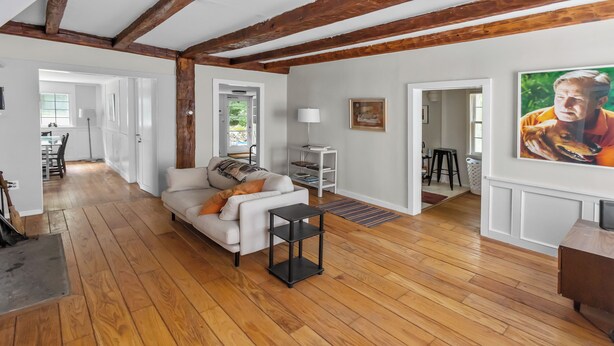 Ein geräumiger Wohnbereich mit Holzboden, einem weißen Sofa, einem schwarzen Beistelltisch und einem Bild an der Wand.