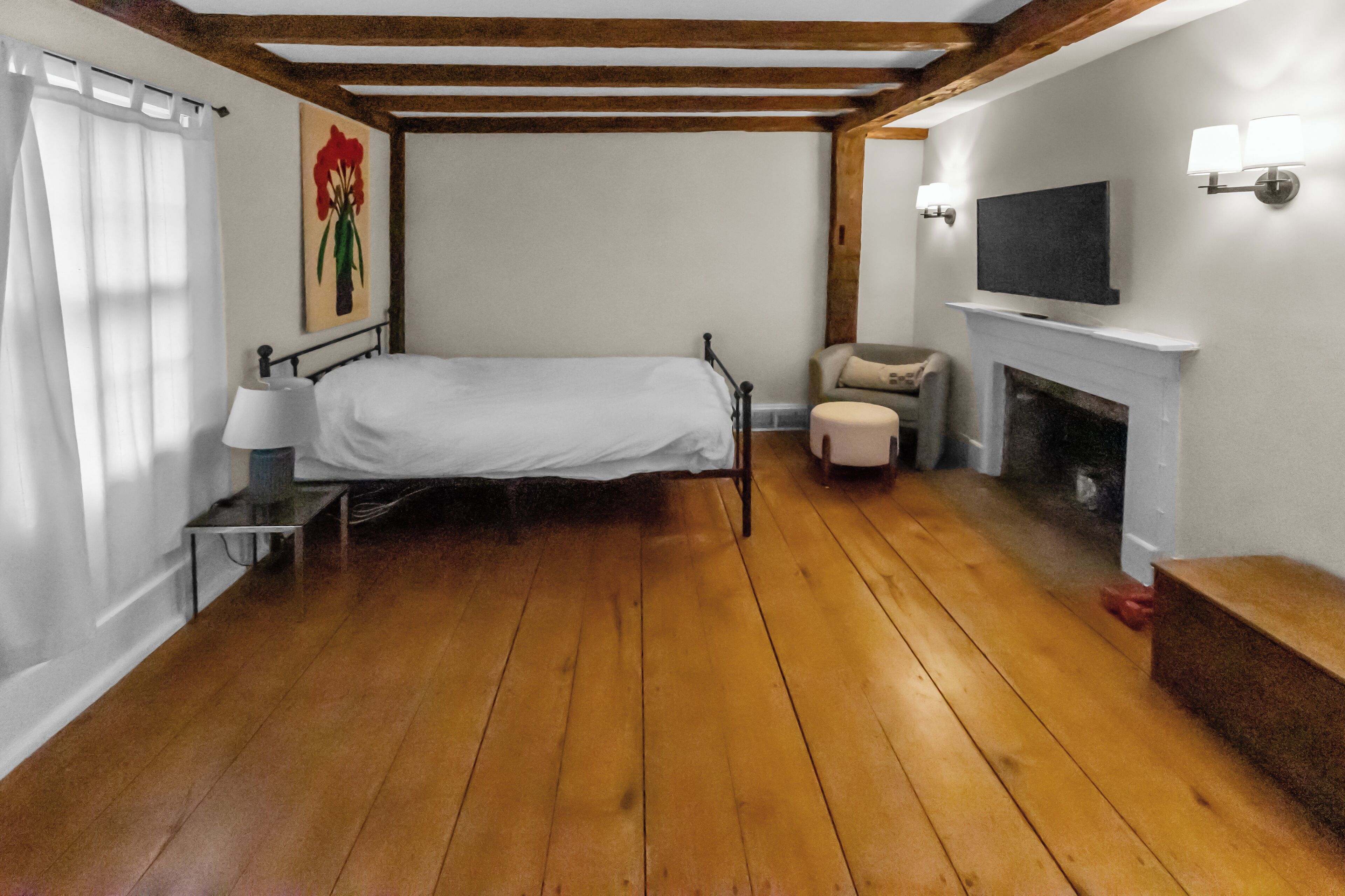 Une chambre avec un plancher en bois, un lit, une chaise, une cheminée et un téléviseur fixé au mur.