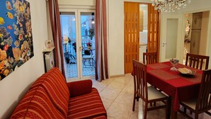 Una sala de estar con sofá, mesa de comedor y sillas. Hay una araña de cristal, un acuario grande y una puerta que da a un balcón.