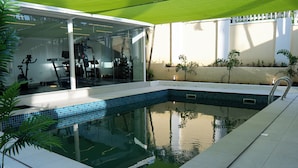 A swimming pool with a glass enclosure, a fitness area with exercise equipment, and a white fence. - Two Bedroom Luxury Apartment in Maitama, Abuja (Abuja)