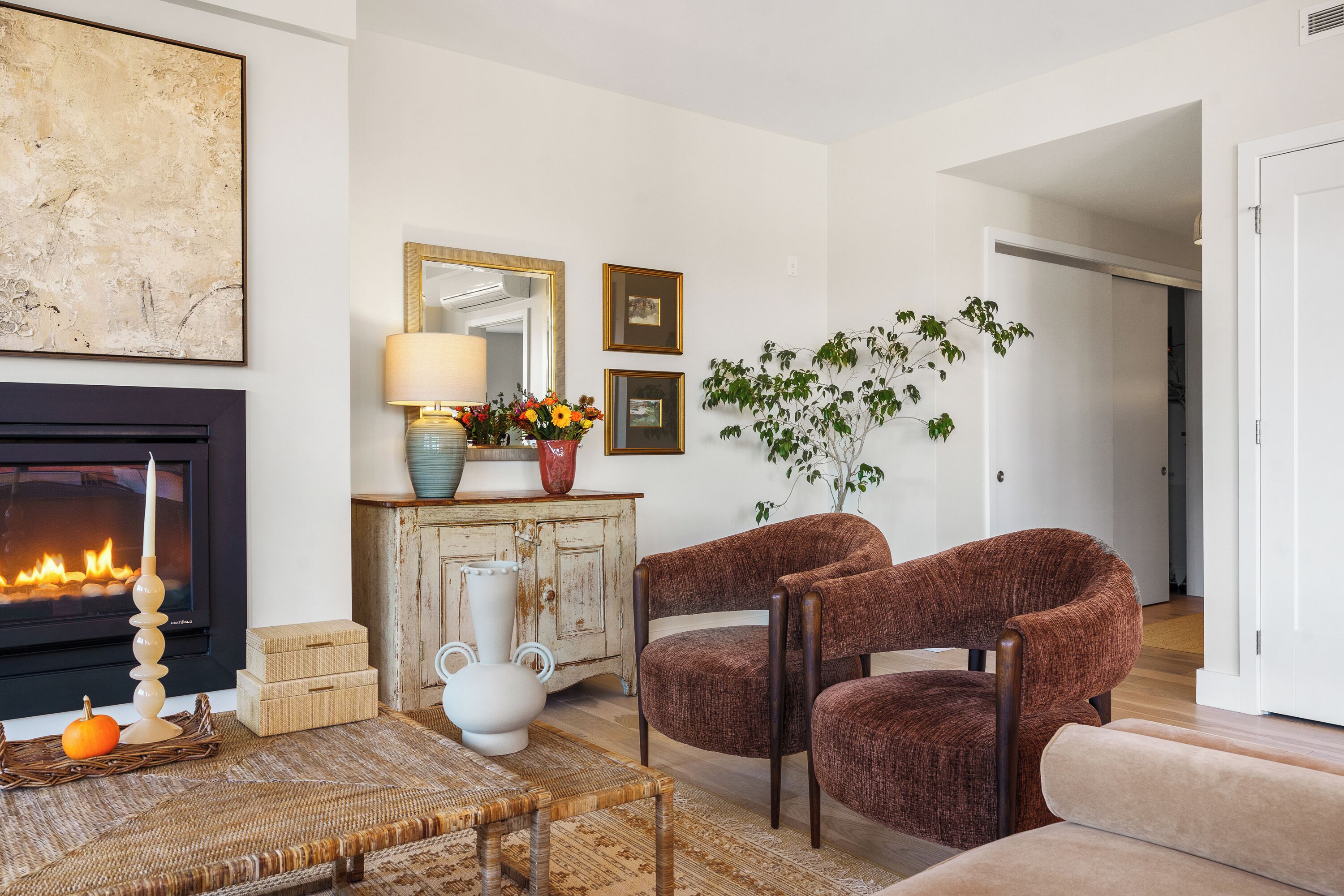 Un salon avec une cheminée, deux fauteuils marron, une table basse et un grand miroir.