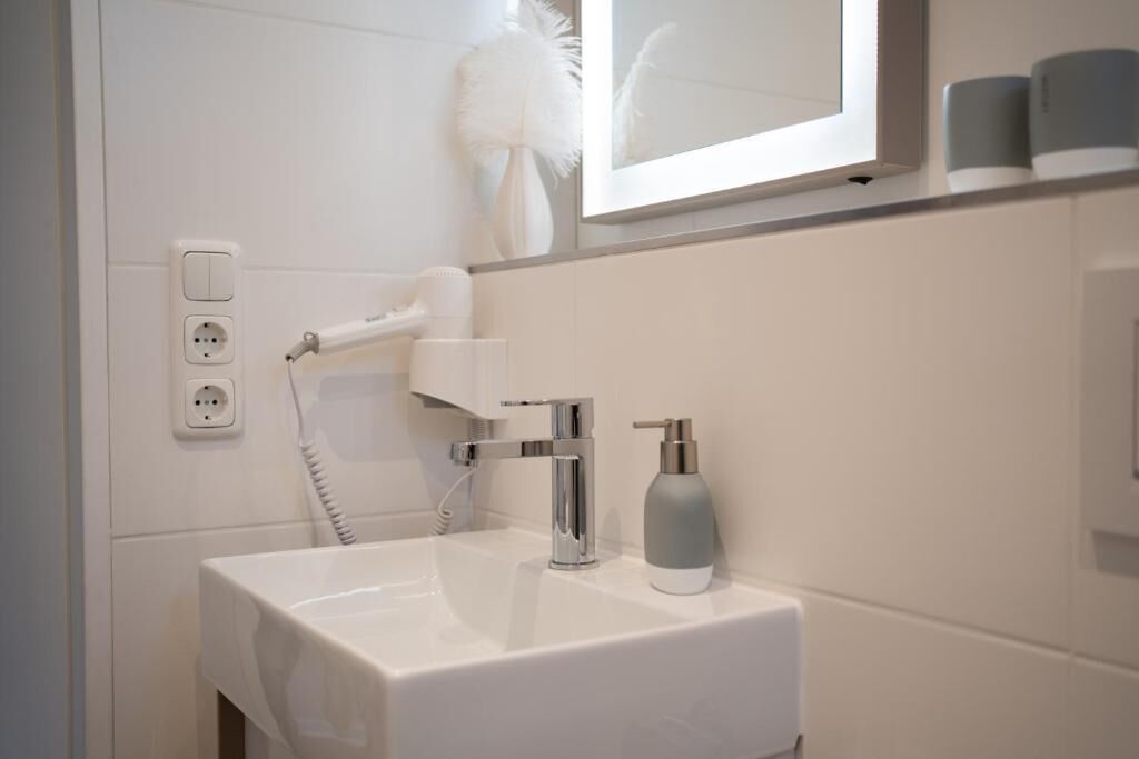 Ein modernes Badezimmer mit einem weißen Waschbecken, einem Handföhn und einem Spiegel über dem Waschbecken.