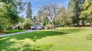 A house with a driveway, surrounded by trees and a well-maintained lawn. - Hideaway Hill lux downtown garden cottage & hottub (Waynesville)
