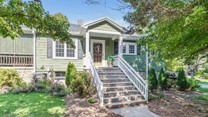 A two-story house with a front porch, a staircase, and a well-maintained garden. - Hideaway Hill lux downtown garden cottage & hottub (Waynesville)