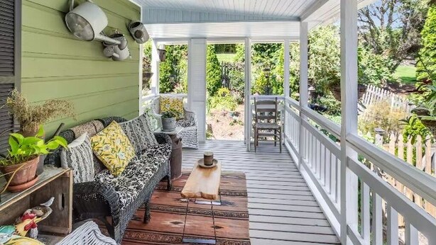 A covered porch with a wooden deck, a sofa with patterned cushions, and a view of a garden. - Hideaway Hill lux downtown garden cottage & hottub (Waynesville)