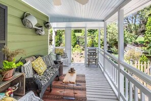 Une véranda avec une terrasse en bois, un canapé agrémenté de coussins à motifs et une vue sur un jardin.