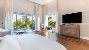 A spacious bedroom with a large bed, a TV mounted on the wall, and a view of palm trees through large windows. - Villa Ametista a Golfer's Dream 5-BD villa in front to Punta Espada Golf Course (Punta Cana)